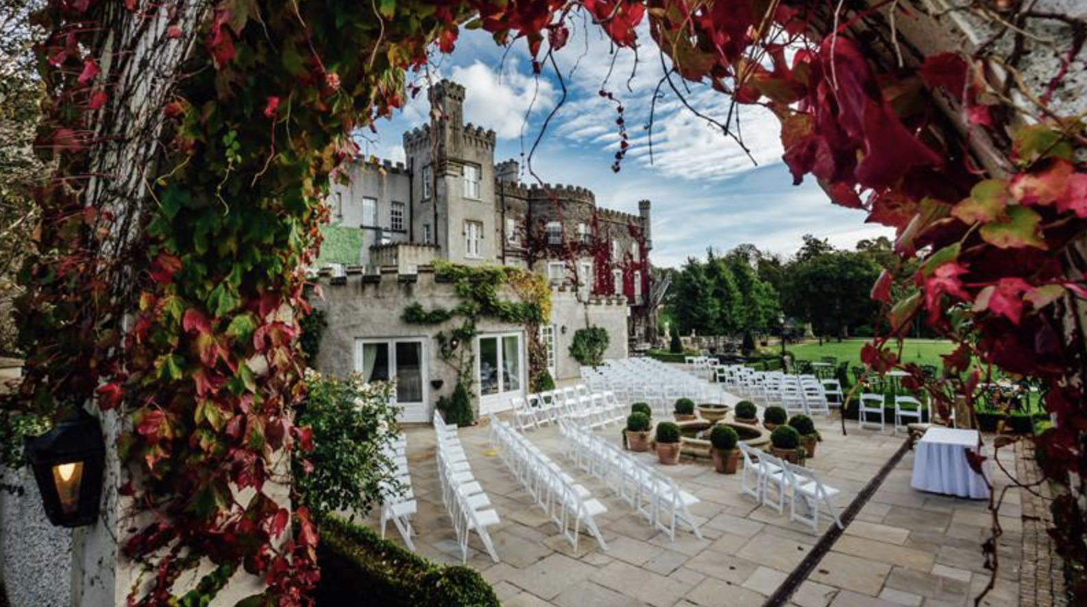Rows of white chairs set for an outdoor ceremony on the castle terrace, framed by autumn vines